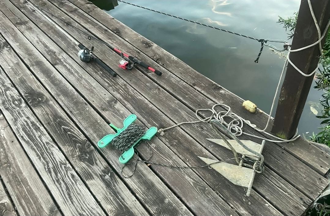 A recovered boat anchor, rope, and fishing rods lying on a Lake Waukomis dock