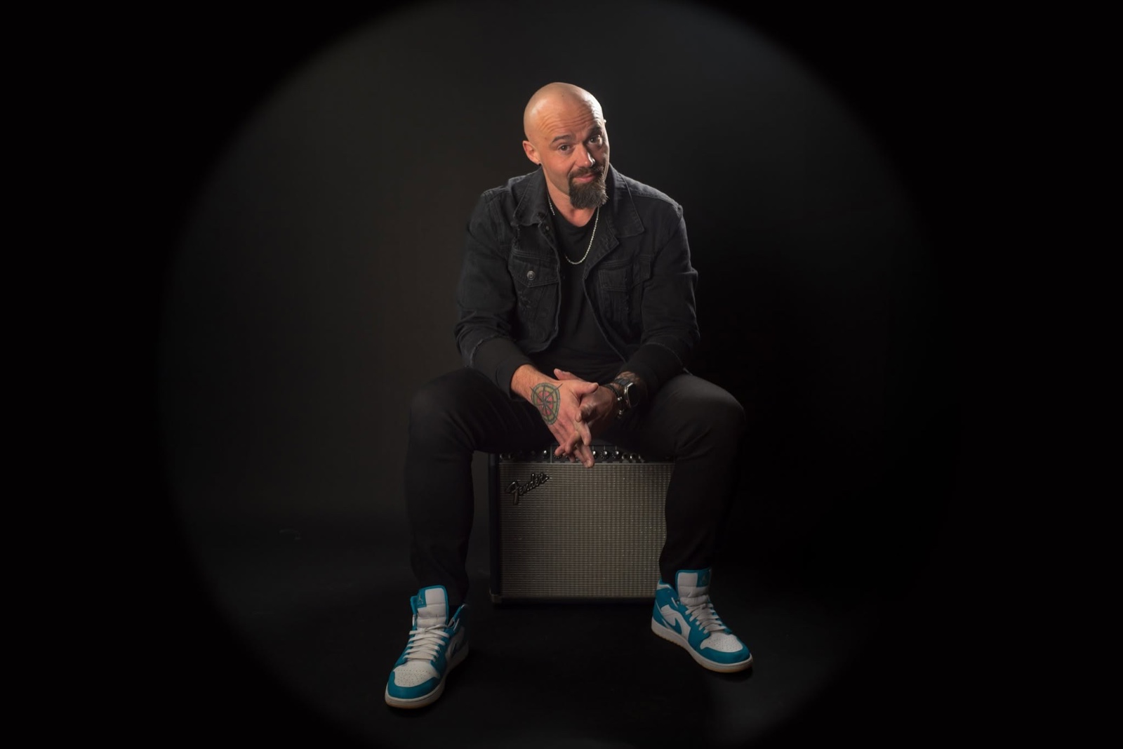 Kansas City performer Miguel Antonio seated on a guitar amplifier against a dark background